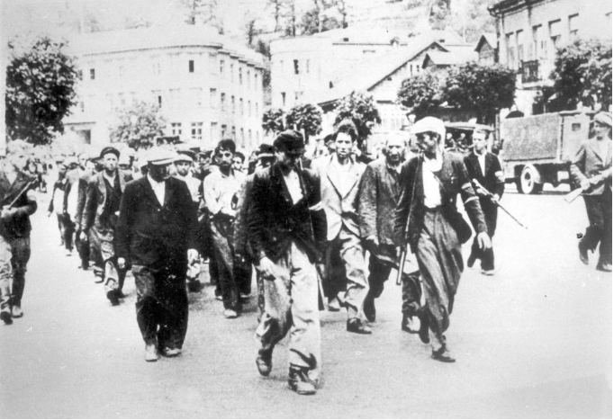 Deportation of Jews across George Maciunas Square under the guard of armed Lithuanians, in the background the Chamber of Agriculture of the Republic of Lithuania (left), June 1941