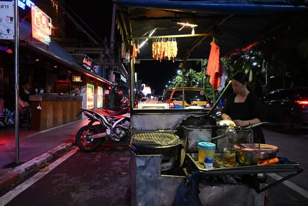 DFC 0508 Late-night street food vendor grilling skewers at a busy city curbside stall neon lights and motorcycles lining the bustling street