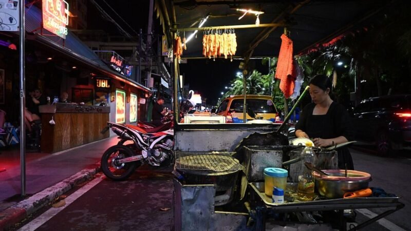 DFC 0508 Late-night street food vendor grilling skewers at a busy city curbside stall neon lights and motorcycles lining the bustling street